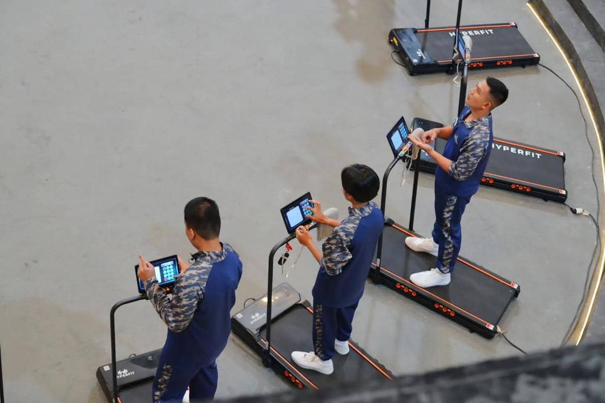 Tiga peserta mengenakan seragam olahraga biru sedang berlari di atas treadmill sambil menjawab soal melalui tablet di acara Clash of Champions.