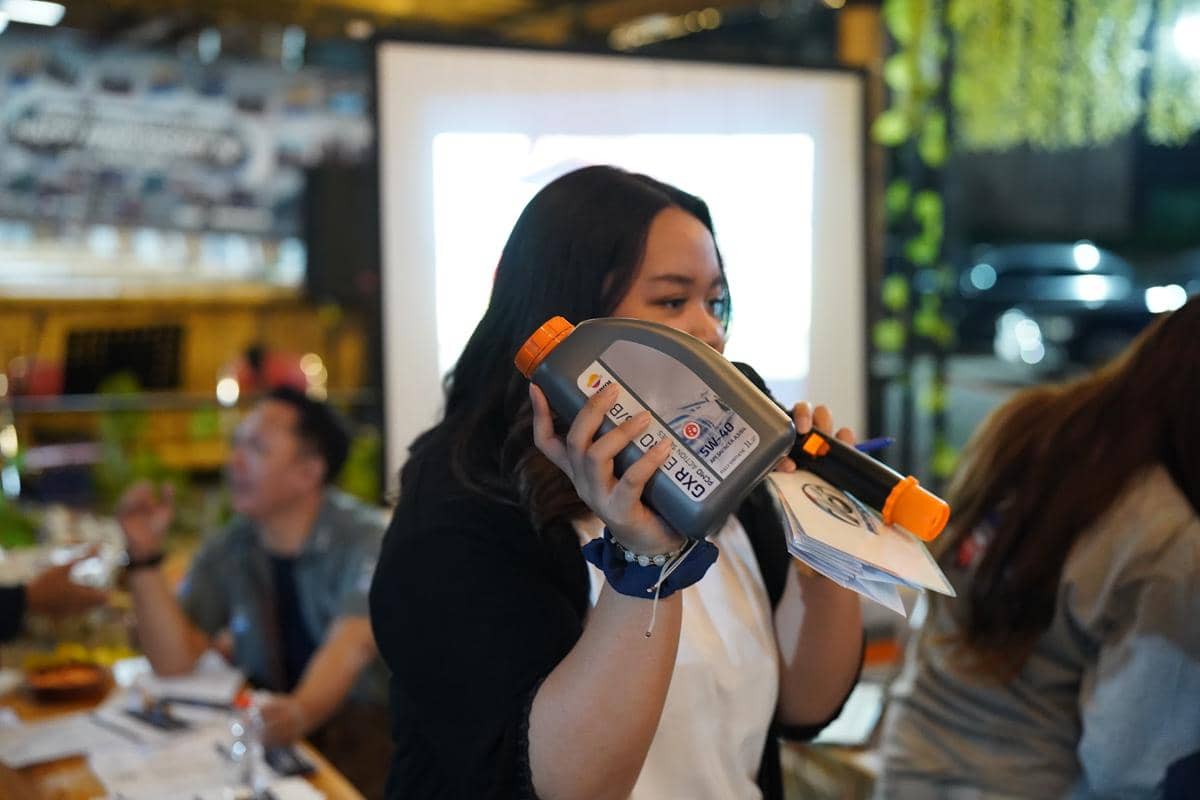 Seorang wanita memegang botol oli Repsol GXR Euro sambil berbicara menggunakan mikrofon di acara peluncuran produk.