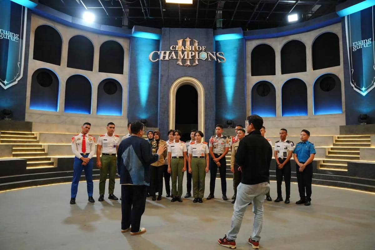 Para peserta berseragam berdiri di panggung acara Clash of Champions dengan latar desain modern berwarna biru dan abu-abu.