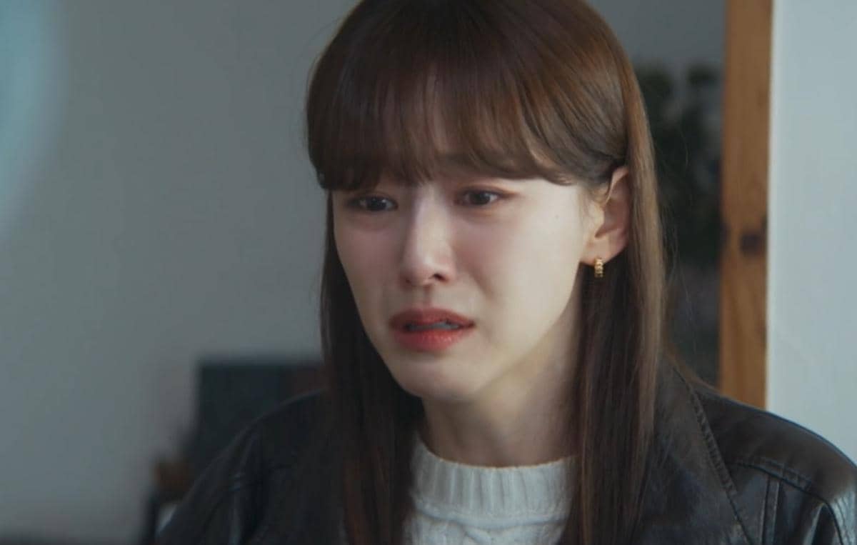 Seorang wanita berambut panjang dengan ekspresi sedih mengenakan jaket kulit hitam dan sweter putih dalam cuplikan drama Korea Reborn Rookie.