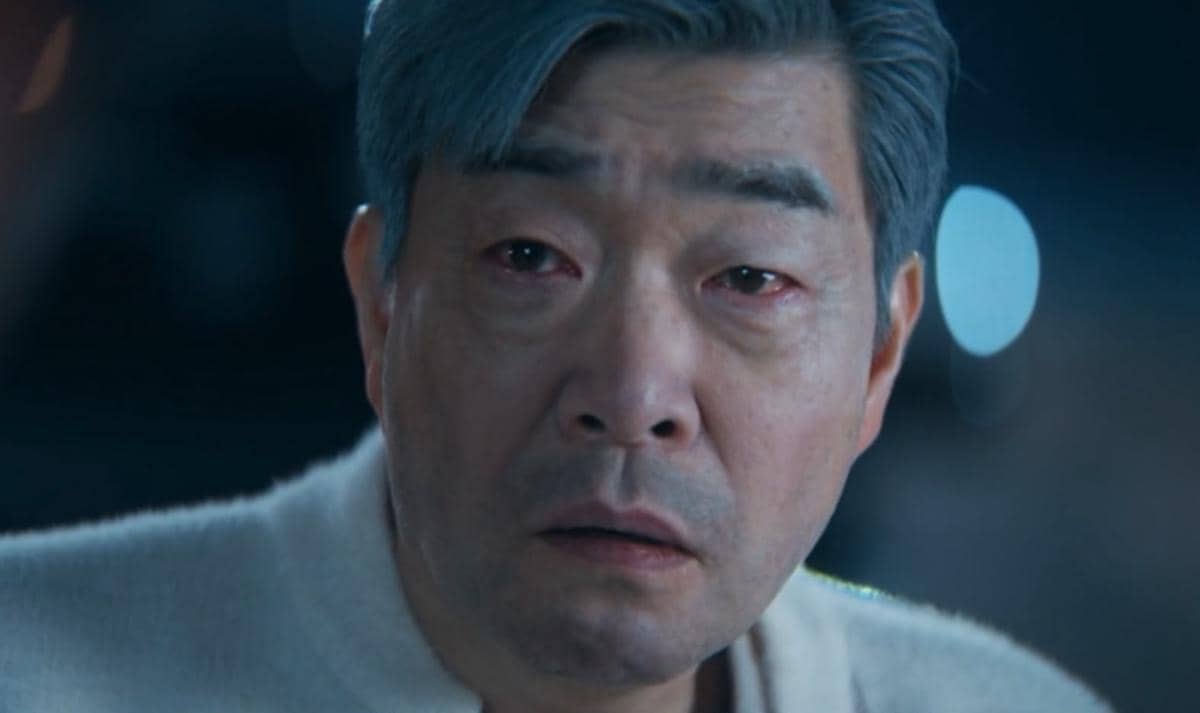 Seorang pria paruh baya berambut abu-abu dengan ekspresi sedih dan mata merah dalam cuplikan drama Korea Reborn Rookie.