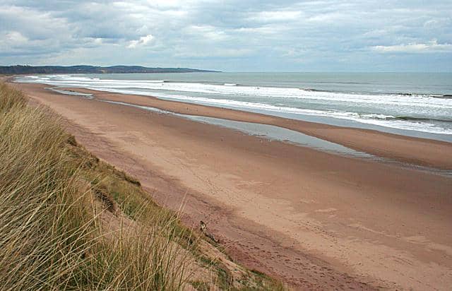 Pemandangan pantai Montrose dengan pasir cokelat luas, ombak lembut, dan langit berawan di tepi laut Skotlandia.