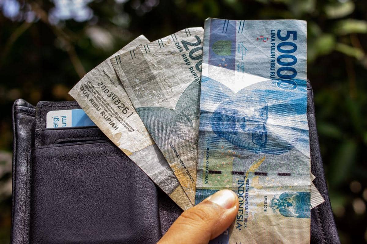ilustrasi seseorang yang memegang uang kertas rupiah Indonesia di luar ruangan bersama dengan dompet