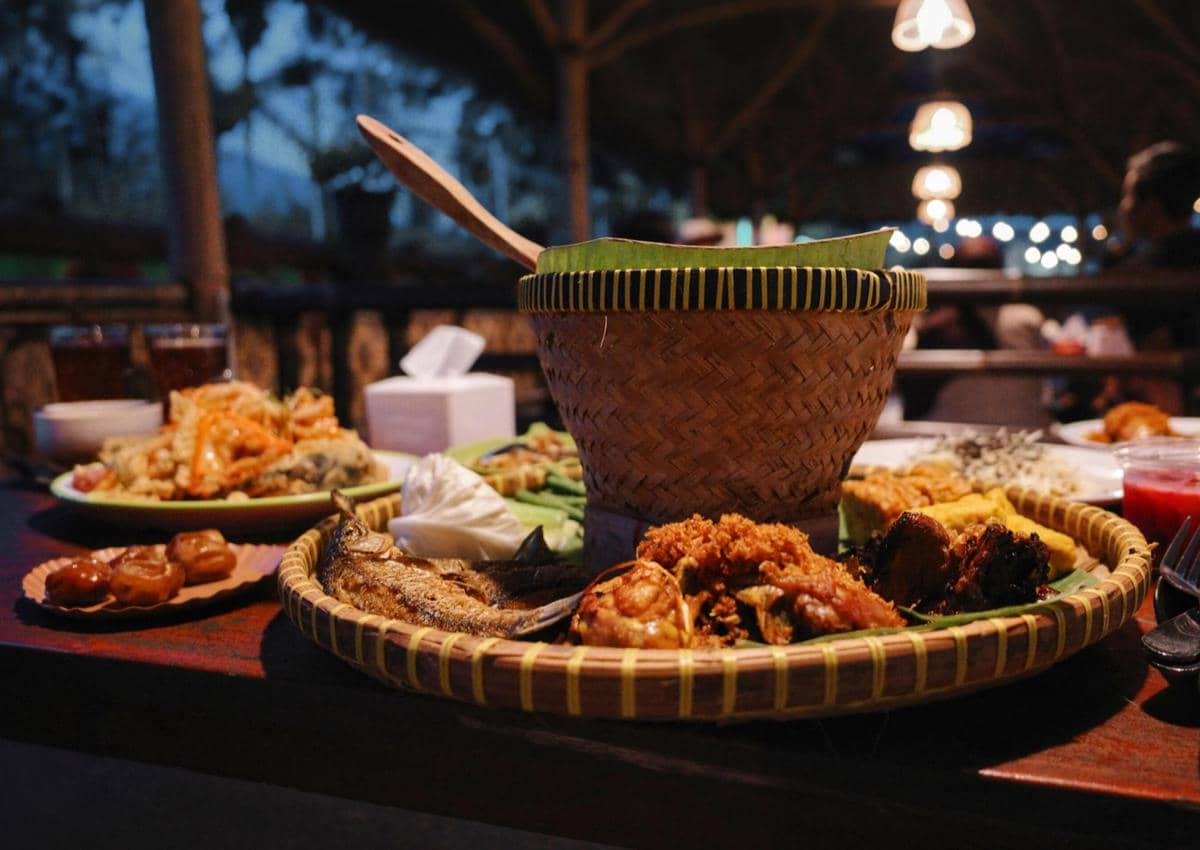 Hidangan tradisional Indonesia tersaji di warung makan dengan nasi dalam bakul anyaman dan lauk seperti ayam goreng serta ikan.