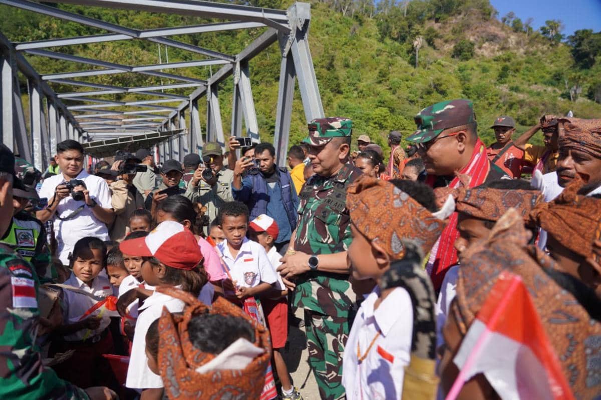 Seorang perwira TNI meninjau pembangunan jembatan di Amfoang, Kupang, bersama anak-anak sekolah dan warga setempat yang mengenakan pakaian adat.