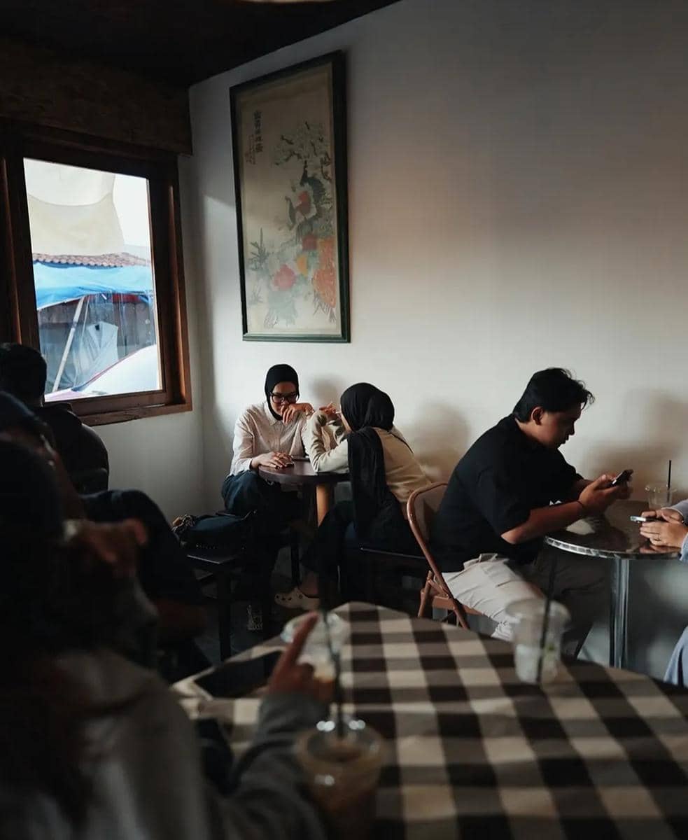 Beberapa pengunjung duduk dan berbincang di dalam Cafe Fatboy Dining Club dengan suasana hangat dan pencahayaan alami dari jendela.