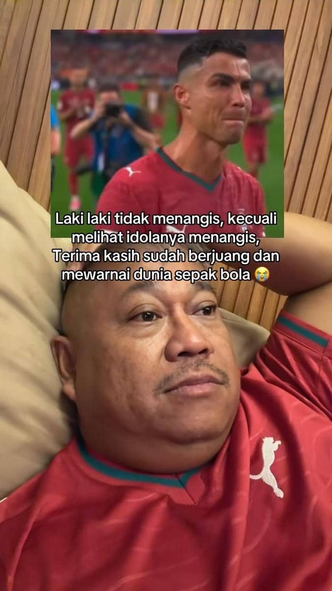 Seorang pria berbaring mengenakan jersey merah menatap layar yang menampilkan pemain sepak bola menangis setelah kekalahan di turnamen besar.