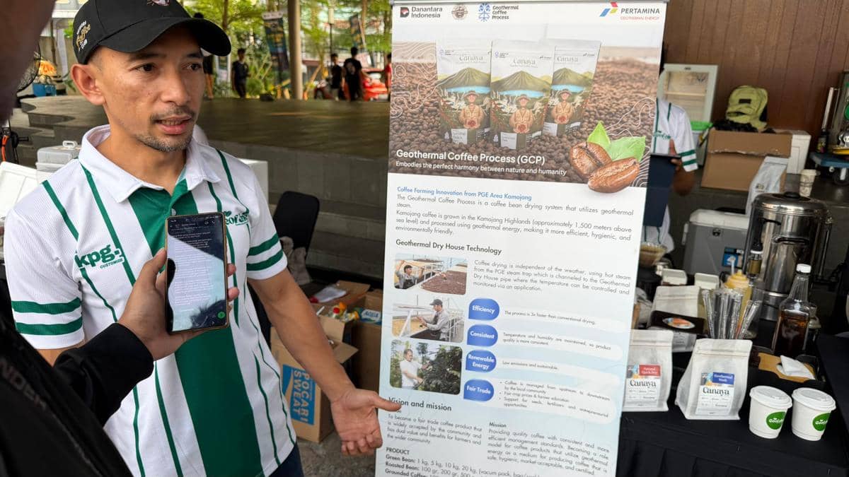 Seorang pria mengenakan seragam berwarna putih hijau menjelaskan tentang Geothermal Coffee Process di Kamojang sambil menunjuk poster informasi produk kopi.