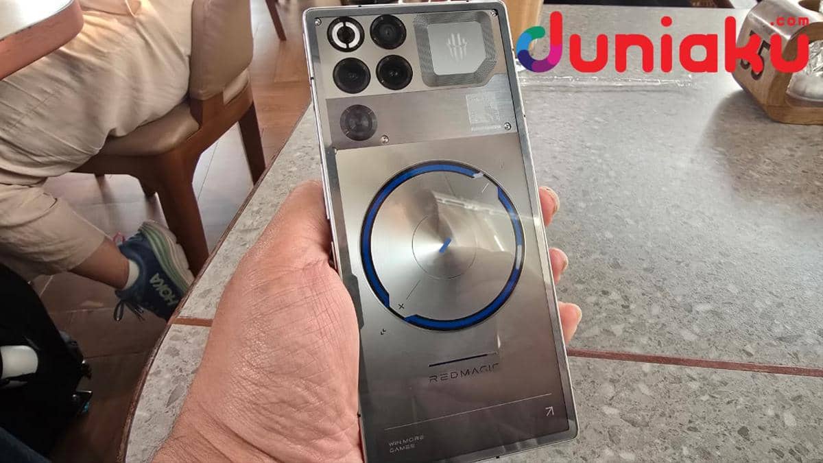 Seseorang memegang ponsel gaming REDMAGIC 11S Pro dengan desain transparan dan cincin biru di bagian belakang.
