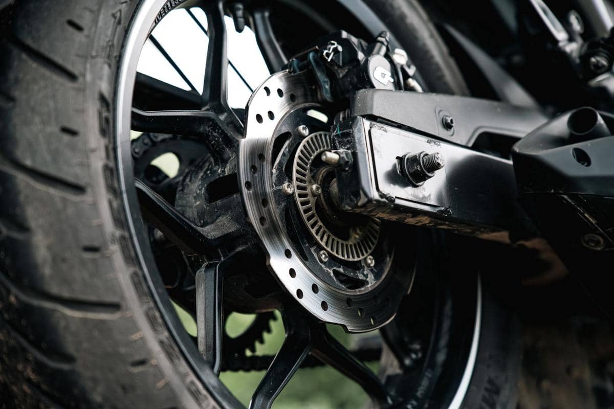 Detail close-up roda belakang motor dengan cakram rem logam dan ban hitam yang tampak kokoh serta bersih.