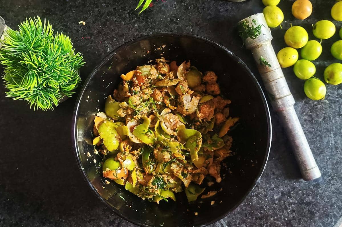 Semangkuk tumis pare ayam dengan potongan pare hijau dan ayam berbumbu di atas meja dapur gelap bersama bahan masakan segar.