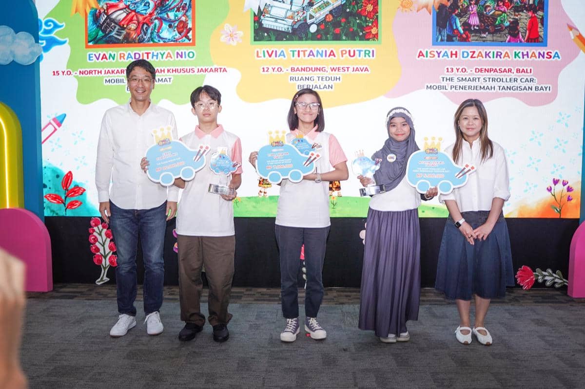 Lima orang berdiri di atas panggung dengan latar warna-warni, tiga di antaranya memegang trofi dan papan penghargaan lomba kreativitas anak.