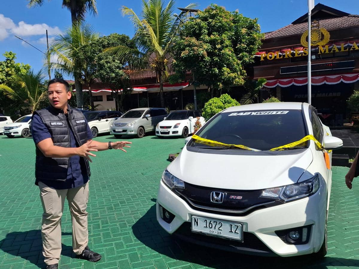 Petugas kepolisian berdiri di samping mobil Honda Jazz putih yang menjadi barang bukti kasus pencurian di Malang.