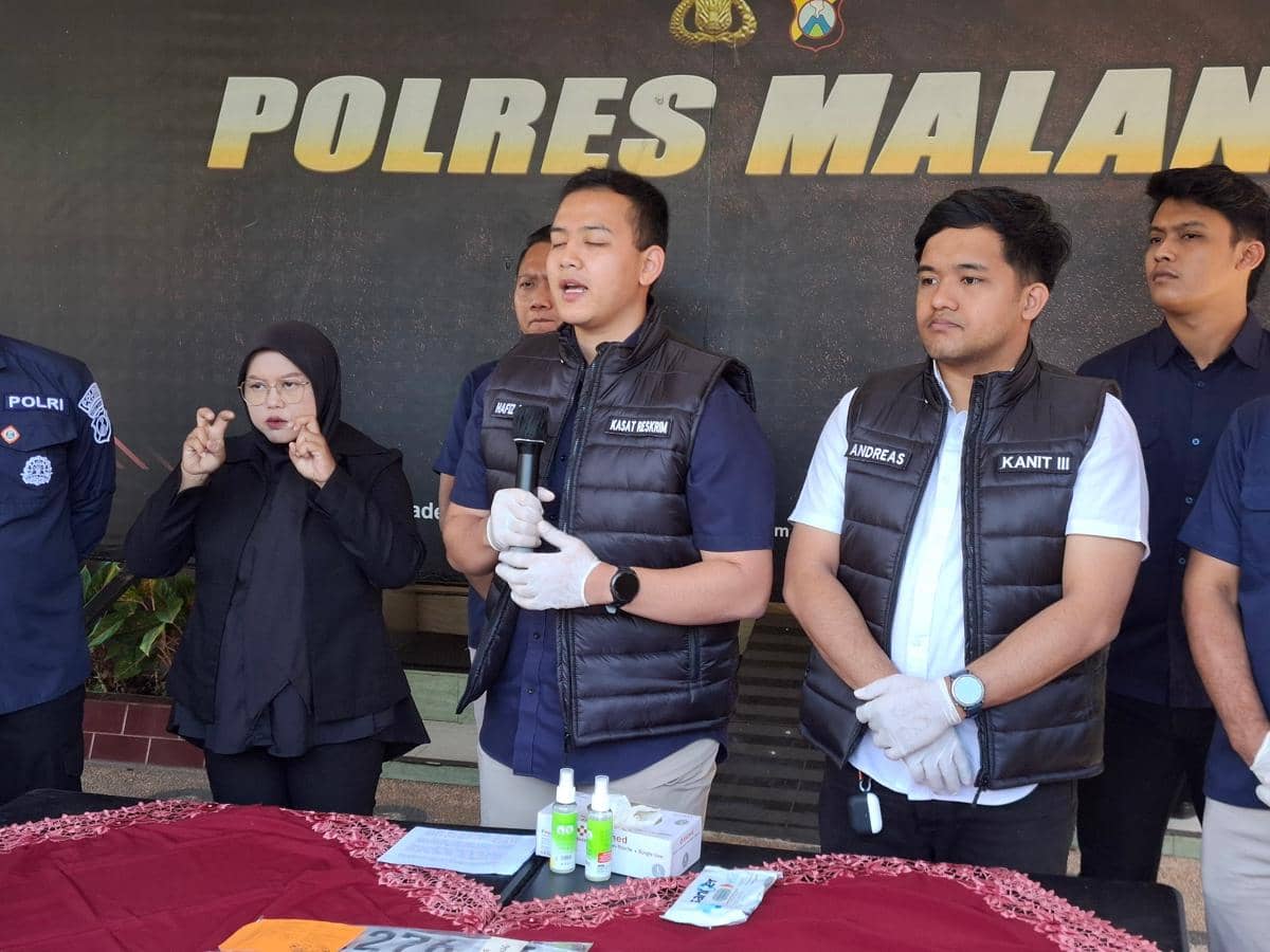 Beberapa petugas kepolisian berdiri di depan backdrop bertuliskan Polres Malang saat konferensi pers dengan barang bukti di atas meja.