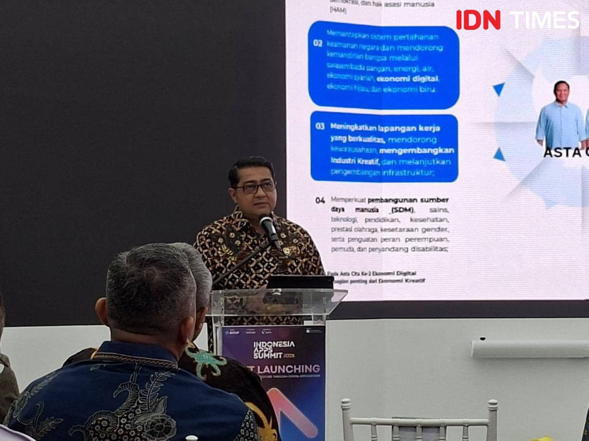 Seorang pria berbicara di podium dengan latar layar presentasi bertema ekonomi digital dan industri kreatif di sebuah acara peluncuran.