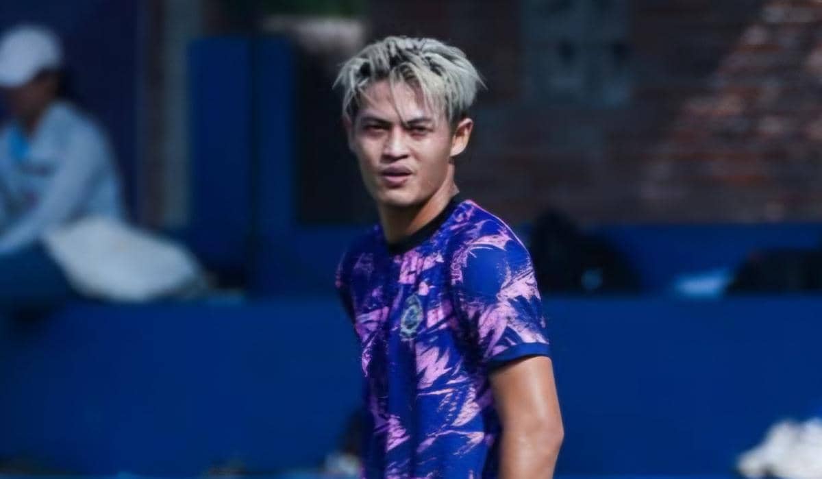 Seorang pemain Arema FC berambut pirang mengenakan jersey latihan ungu bermotif saat berada di lapangan latihan.