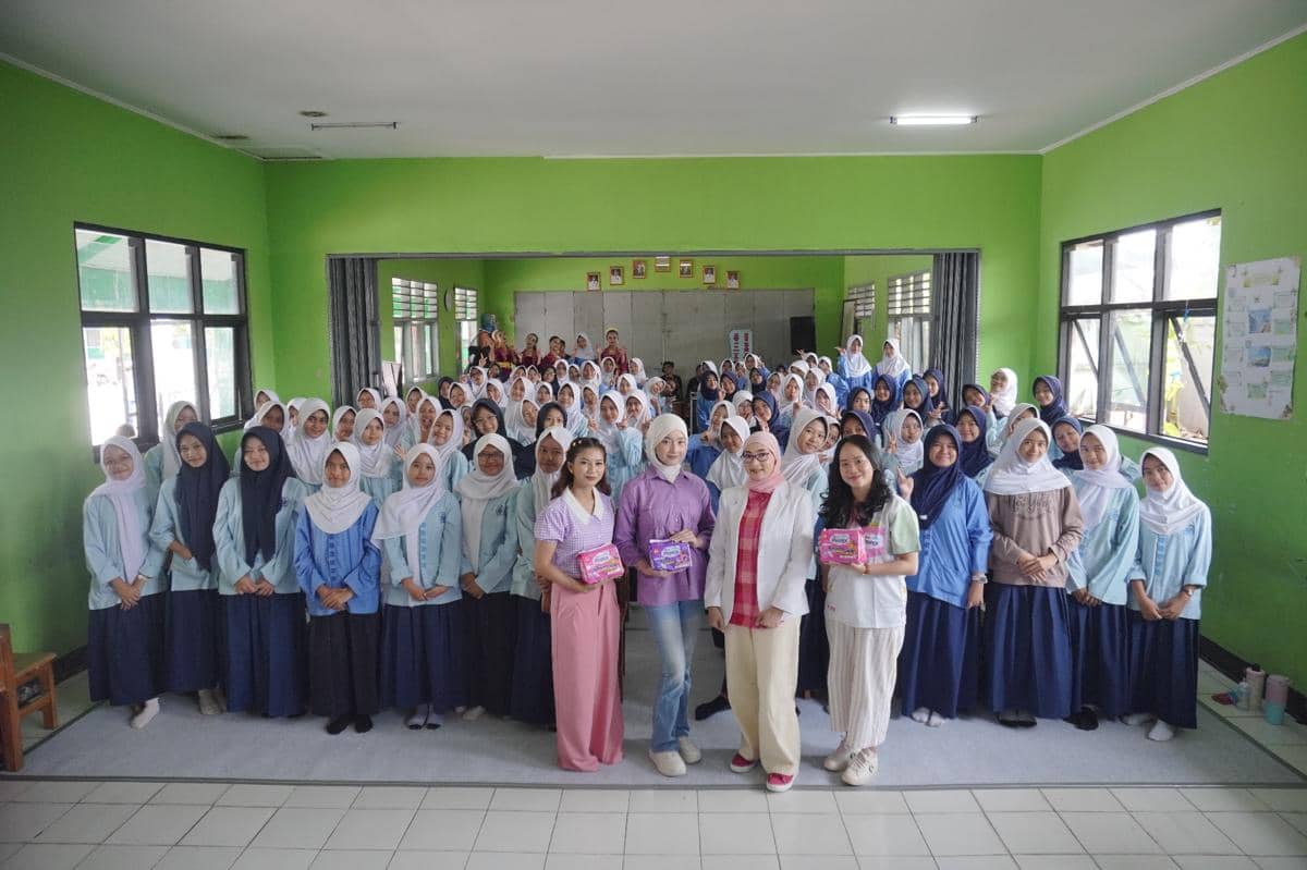 Sejumlah siswi sekolah berpose bersama tim Hers Protex dalam kegiatan edukasi kesehatan di ruang kelas berwarna hijau.