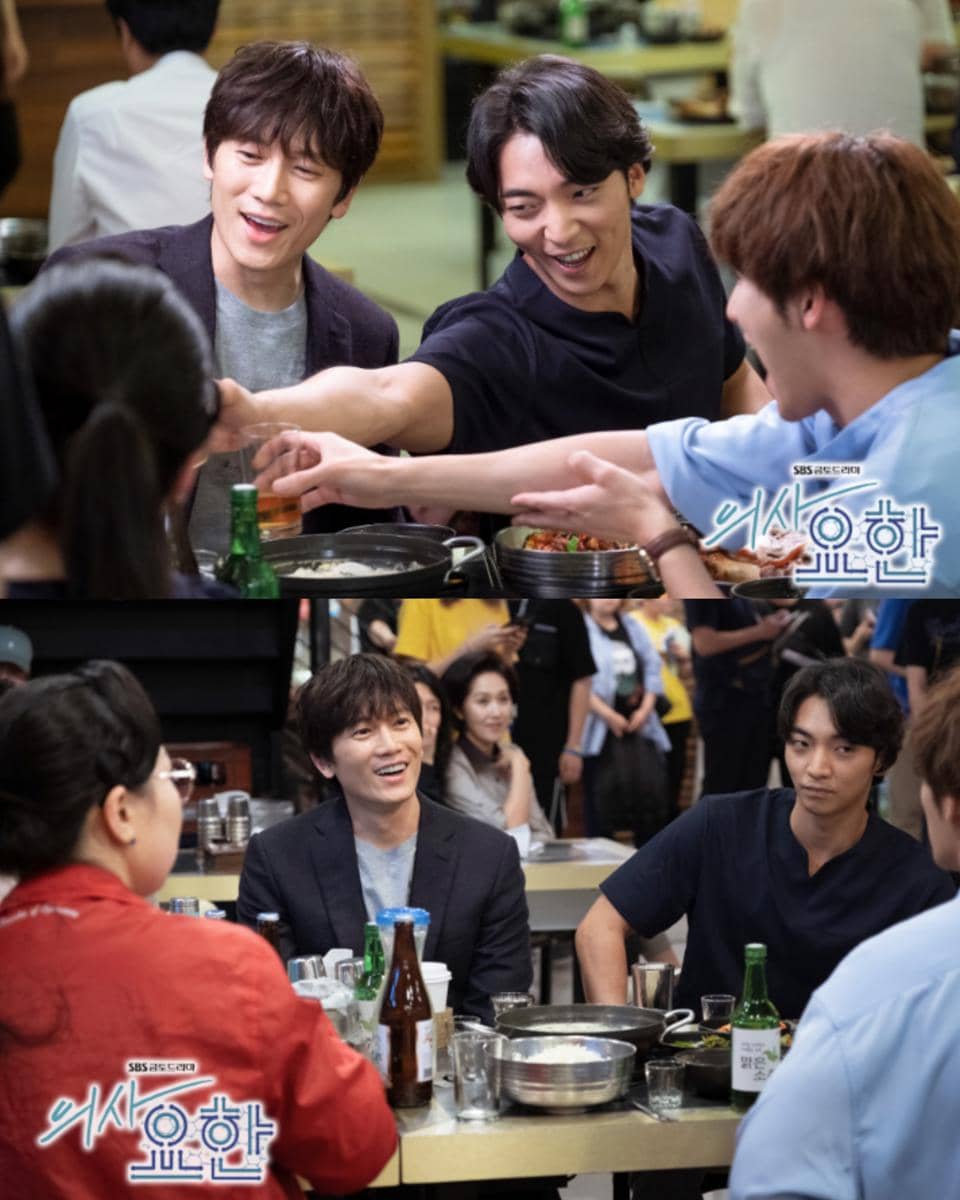 Beberapa aktor sedang duduk di meja restoran sambil tertawa dan bersulang dalam adegan drama Korea Doctor John.