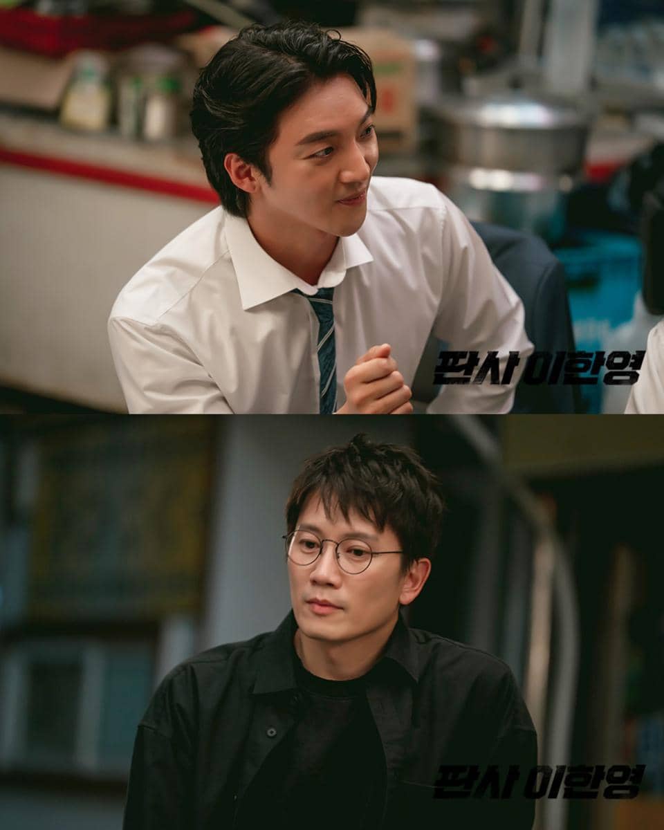 Dua aktor dalam adegan drama The Judge Returns, satu mengenakan kemeja putih dengan dasi dan satu lagi mengenakan kemeja hitam serta kacamata.