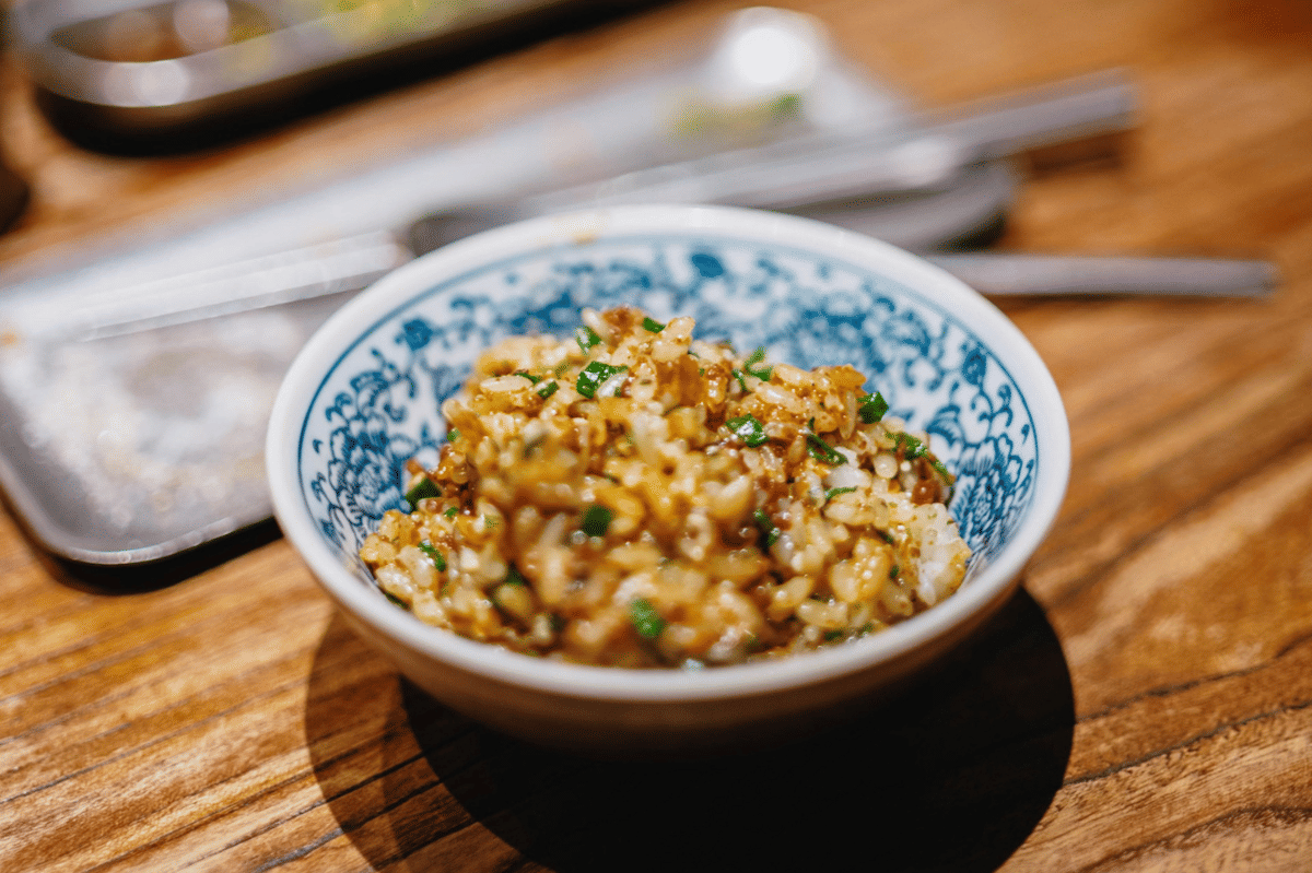 Semangkuk niku miso zosui disajikan di atas meja kayu, berisi nasi dengan potongan daging dan taburan daun bawang segar.