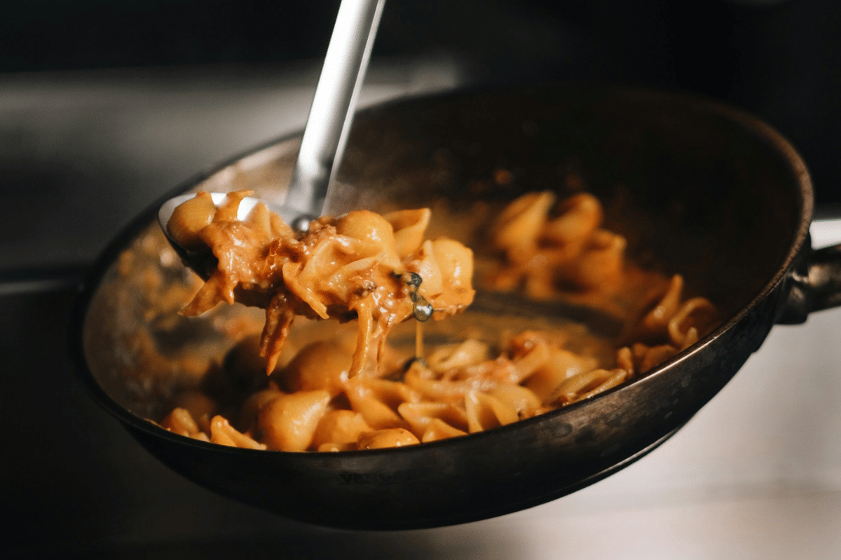 Pasta gochujang alfredo berwarna krem keoranyean dimasak dalam wajan dengan saus kental dan tekstur lembut yang menggugah selera.