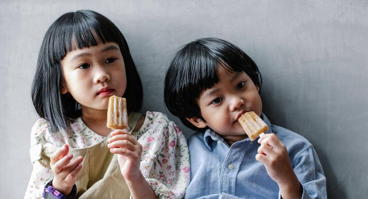 Seorang anak kecil sedang makan es krim sebagai camilan manis yang menggambarkan kebiasaan menikmati makanan penutup.