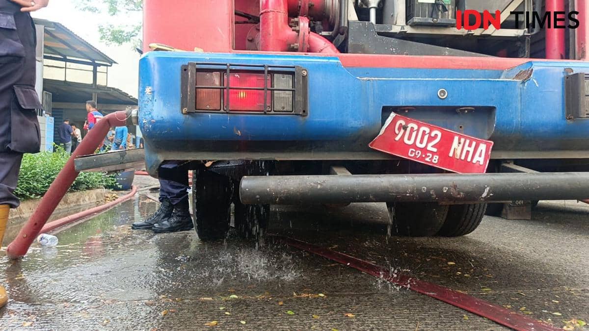 Bagian belakang mobil pemadam kebakaran Tangsel dengan plat nomor miring dan air bocor dari bawah kendaraan di area garasi.