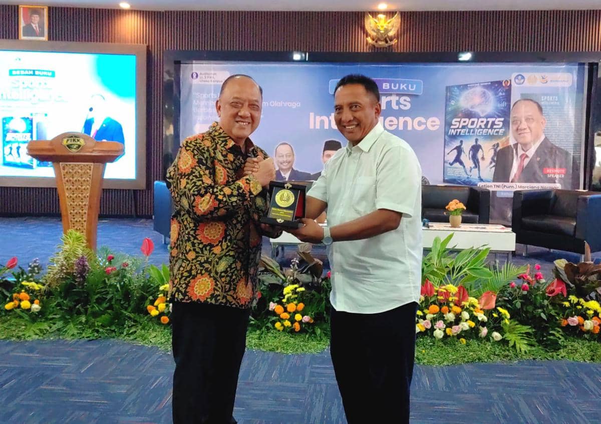 Dua pria berjabat tangan sambil memegang plakat dalam acara peluncuran dan bedah buku Sports Intelligence di UNESA.