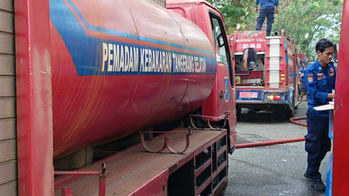 Petugas pemadam kebakaran Tangerang Selatan berdiri di samping armada truk pemadam berwarna merah yang tampak usang di area garasi.