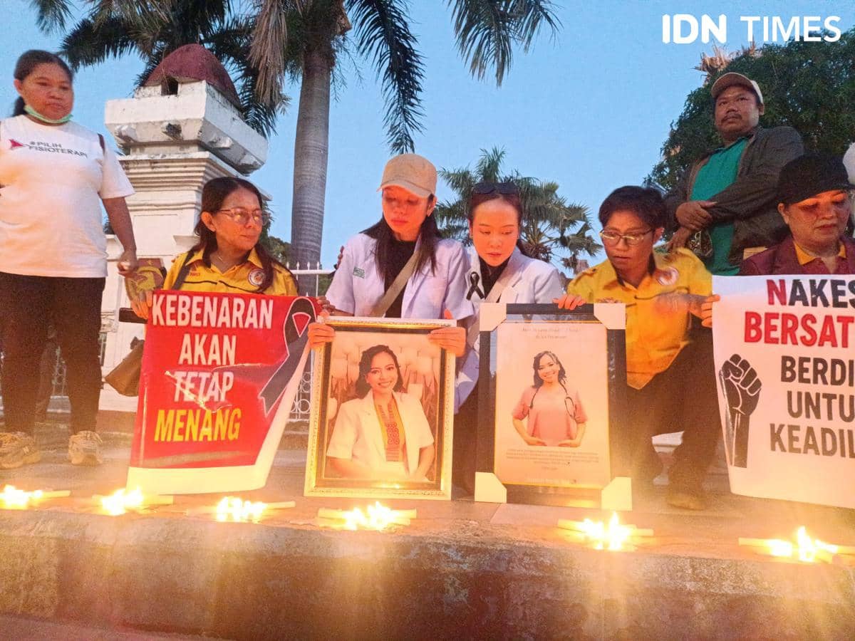 Sejumlah orang menyalakan lilin dan memegang poster bertuliskan pesan keadilan serta foto seorang perempuan di depan gedung DPRD NTT.