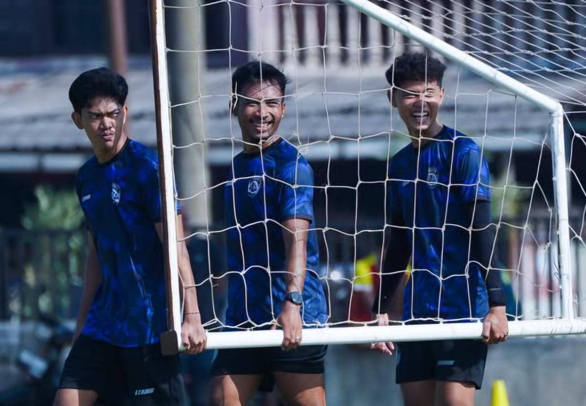 Tiga pemain Arema FC mengenakan seragam latihan biru sambil mengangkat gawang kecil di lapangan saat sesi latihan tim.