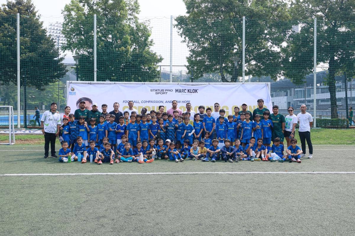 Anak-anak peserta coaching clinic sepak bola berpose bersama pelatih dan panitia di lapangan hijau dengan latar spanduk Marc Klok Foundation.