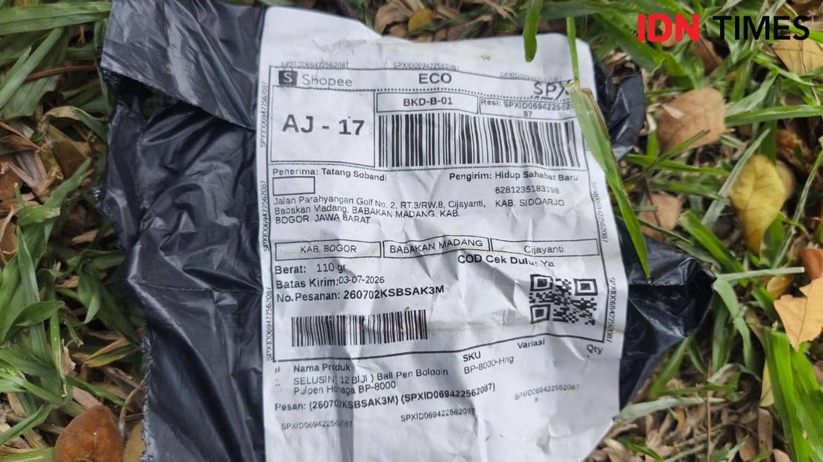 Paket berbungkus plastik hitam dengan label pengiriman Shopee atas nama penerima di Babakan Madang, Bogor, tergeletak di atas rumput.