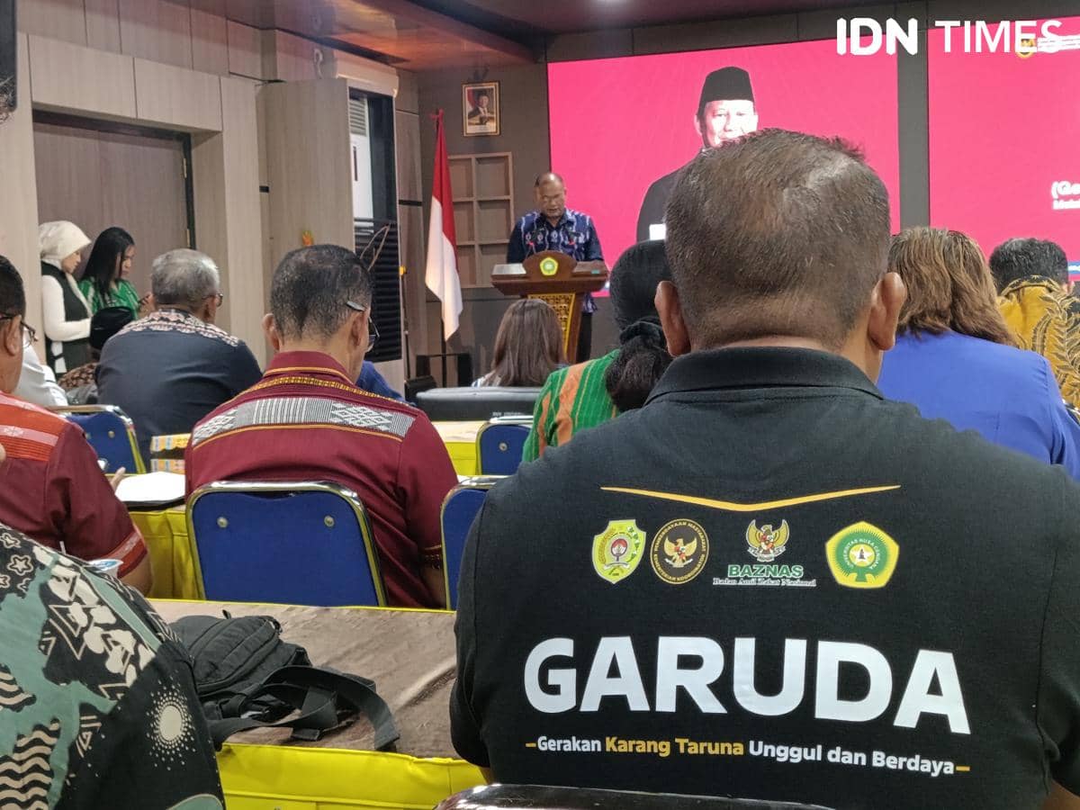 Seorang peserta mengenakan kaus bertuliskan Garuda duduk di aula bersama peserta lain saat acara Program Garuda berlangsung.