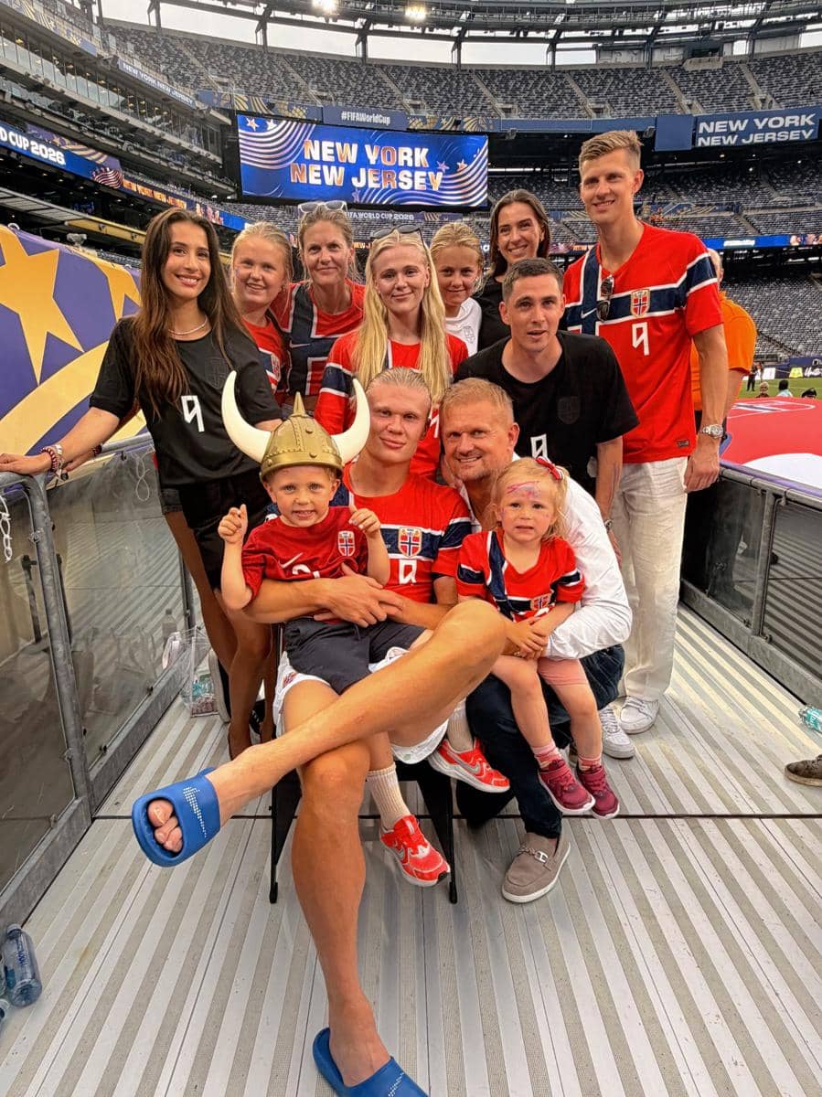 Sekelompok orang mengenakan jersey Norwegia berfoto bersama di stadion dengan latar belakang papan bertuliskan New York New Jersey.