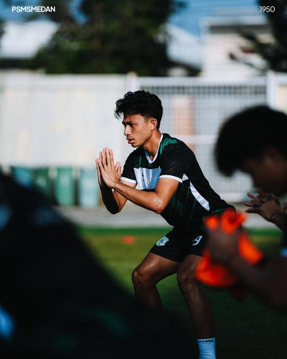Seorang pemain PSMS Medan mengenakan seragam latihan hijau hitam sedang berlatih di lapangan dengan fokus dan posisi setengah jongkok.