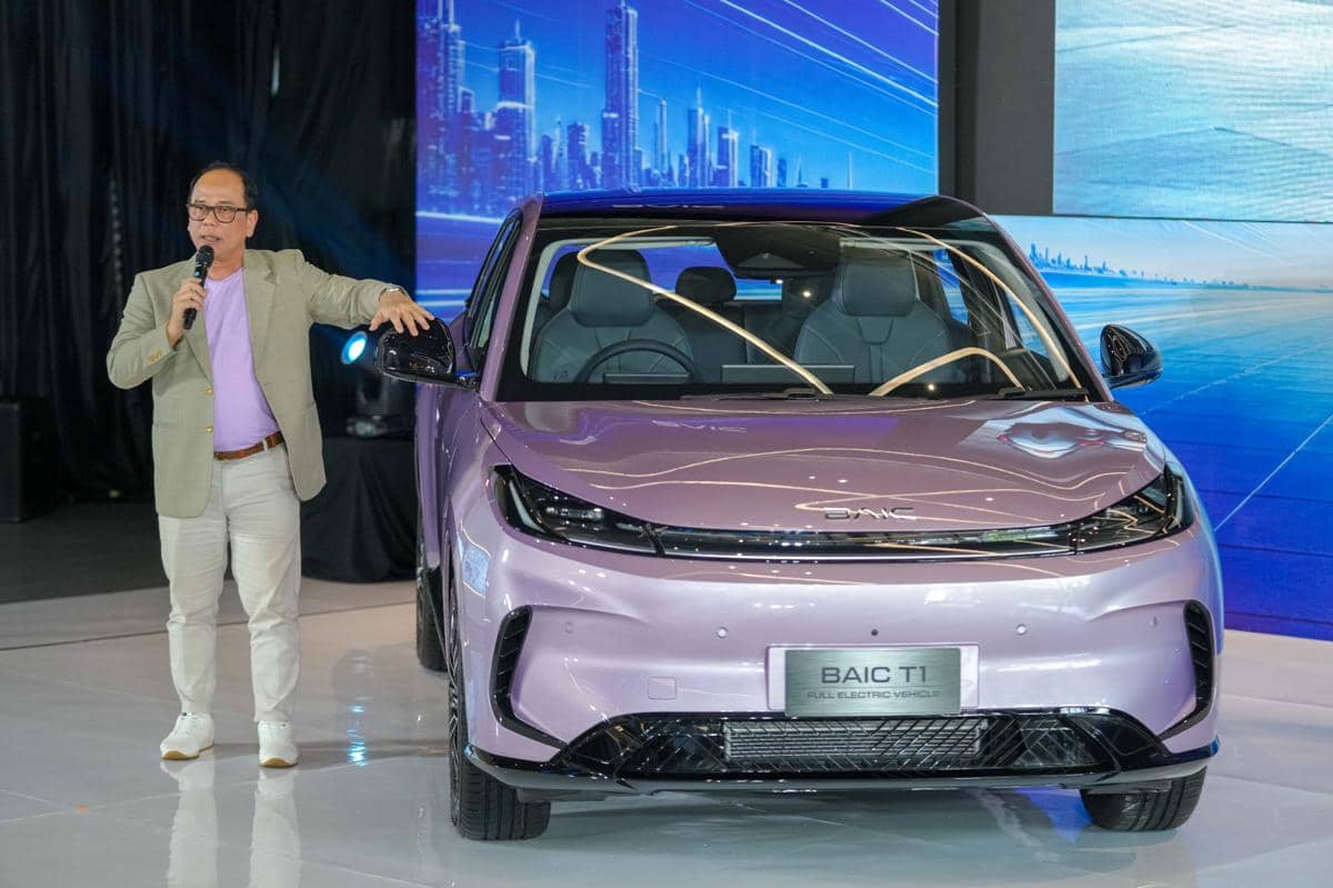 Seorang pria berbicara di atas panggung sambil berdiri di samping mobil listrik BAIC T1 berwarna ungu saat acara peluncuran di Indonesia.