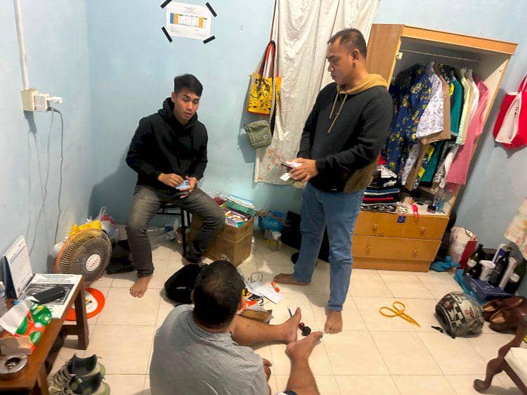 Petugas kepolisian mengamankan seorang pria di dalam kamar yang berantakan dengan berbagai barang berserakan di lantai.