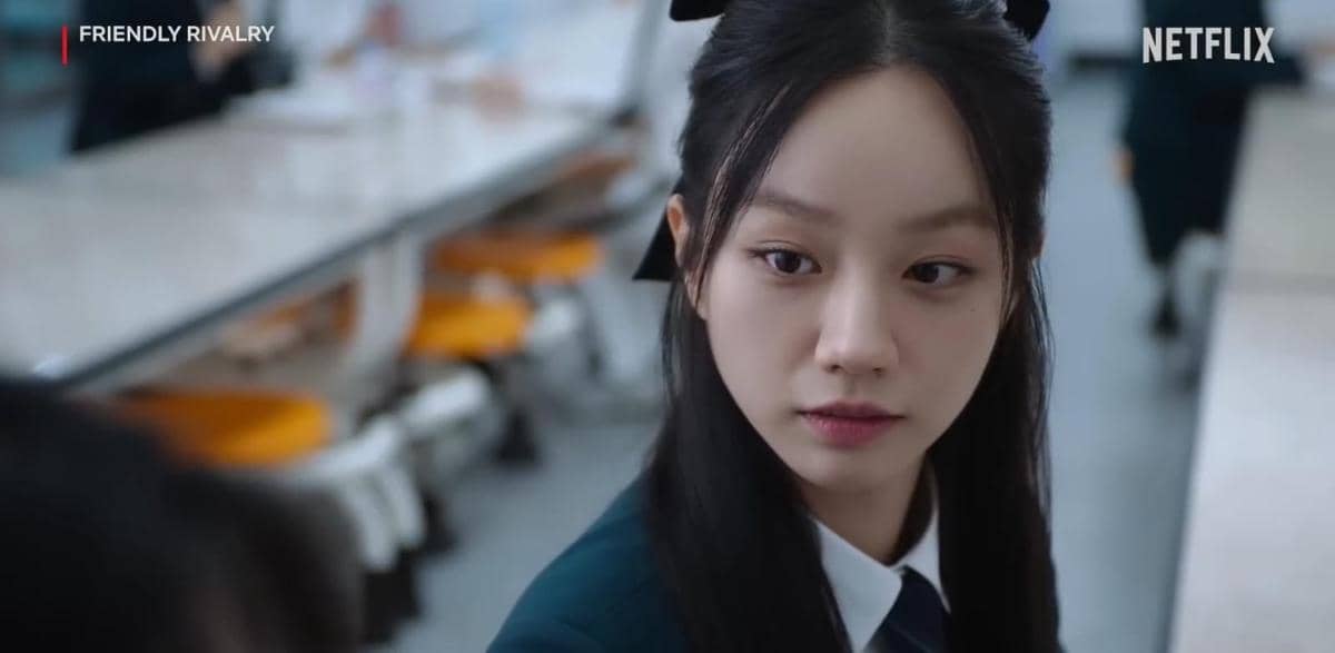Seorang siswi berseragam sekolah duduk di ruang makan sekolah dalam cuplikan drama Friendly Rivalry di Netflix.