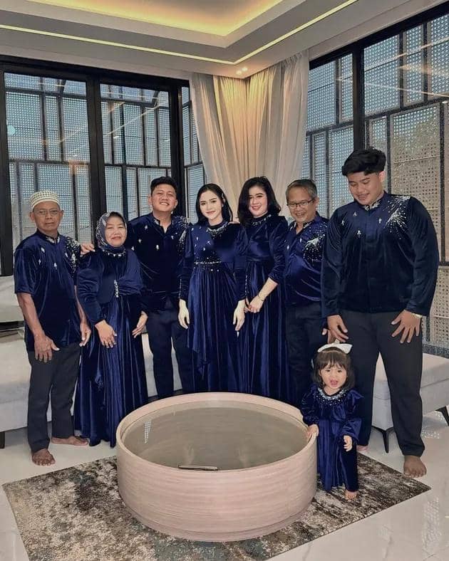 Keluarga berpose bersama di ruang tamu dengan busana seragam berwarna biru tua, terdiri dari pria, wanita, dan anak kecil.
