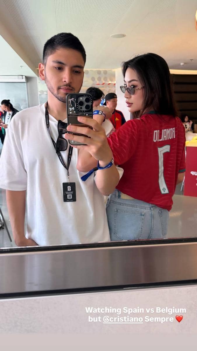 Dua orang berfoto di cermin, pria mengenakan kaus putih dan wanita memakai jersey sepak bola berwarna merah dengan nama Ronaldo di bagian belakang.