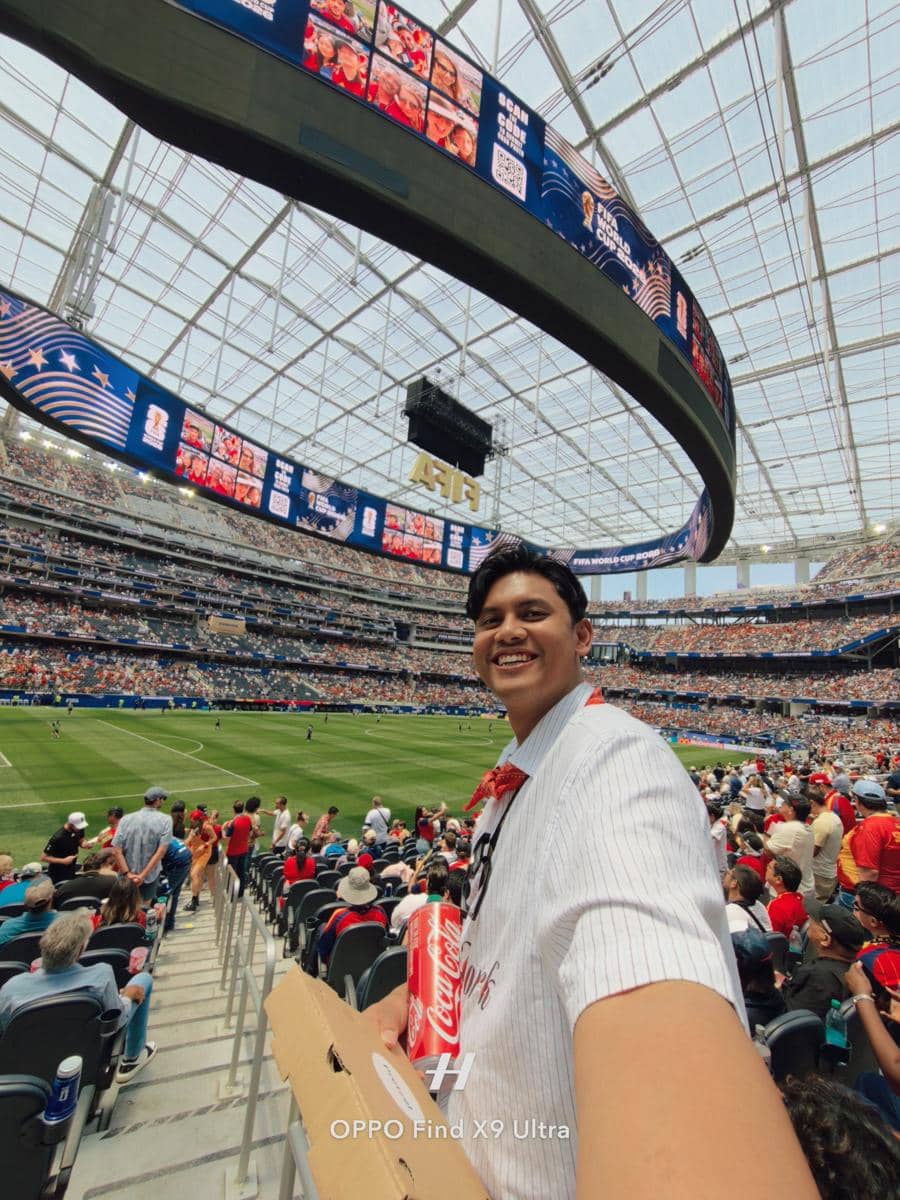 Seorang penonton tersenyum sambil memegang minuman dan makanan di stadion besar saat pertandingan sepak bola Spanyol vs Belgia berlangsung.