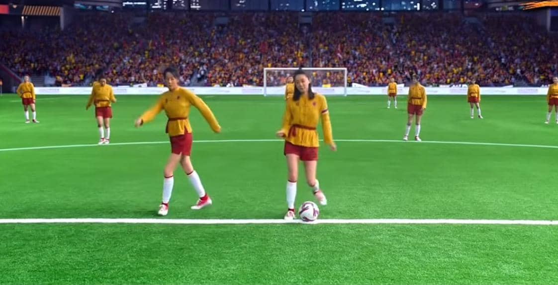 Para pemain sepak bola dengan seragam kuning dan merah tampak bertingkah lucu di lapangan saat kick-off di depan penonton stadion.