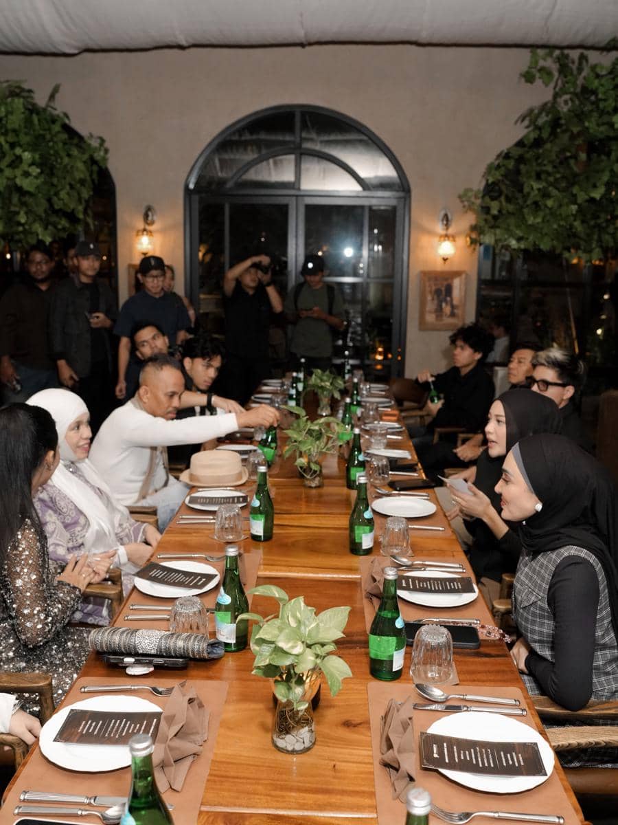 Suasana makan malam ulang tahun di restoran dengan meja panjang, tamu duduk berhadapan menikmati acara dalam suasana hangat dan elegan.