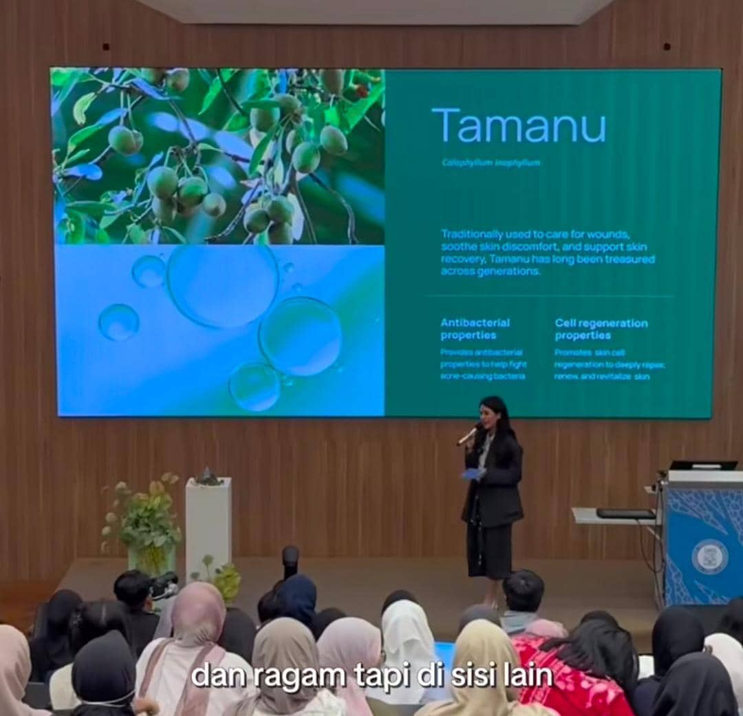 Seorang dosen tamu memberikan presentasi tentang tanaman Tamanu di hadapan mahasiswa di aula ITB dengan layar besar berisi materi ilmiah.