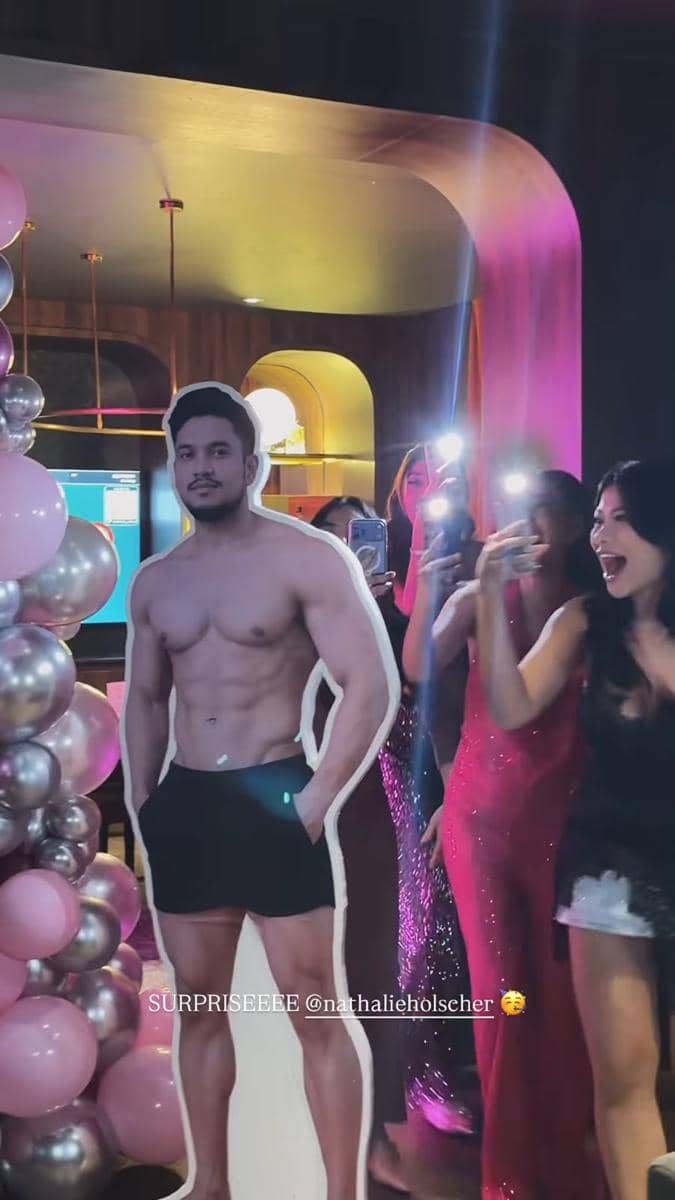 Beberapa wanita tertawa dan berfoto di acara bridal shower dengan dekorasi balon serta potongan kardus pria bertelanjang dada.
