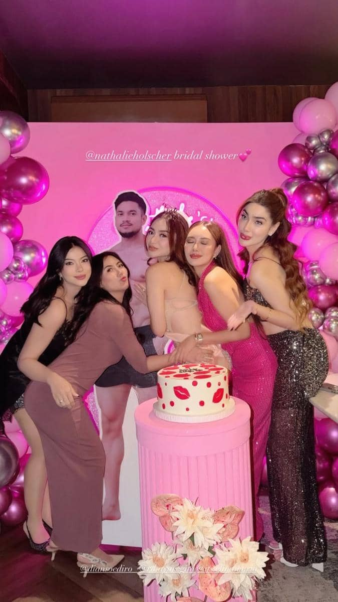 Lima wanita berpose ceria di pesta bridal shower bertema merah muda dengan balon, kue berhias motif bibir, dan dekorasi bunga.