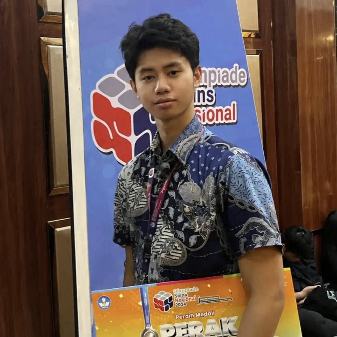 Seorang peserta muda mengenakan batik biru memegang piagam medali perak di ajang Olimpiade Sains Nasional 2024.