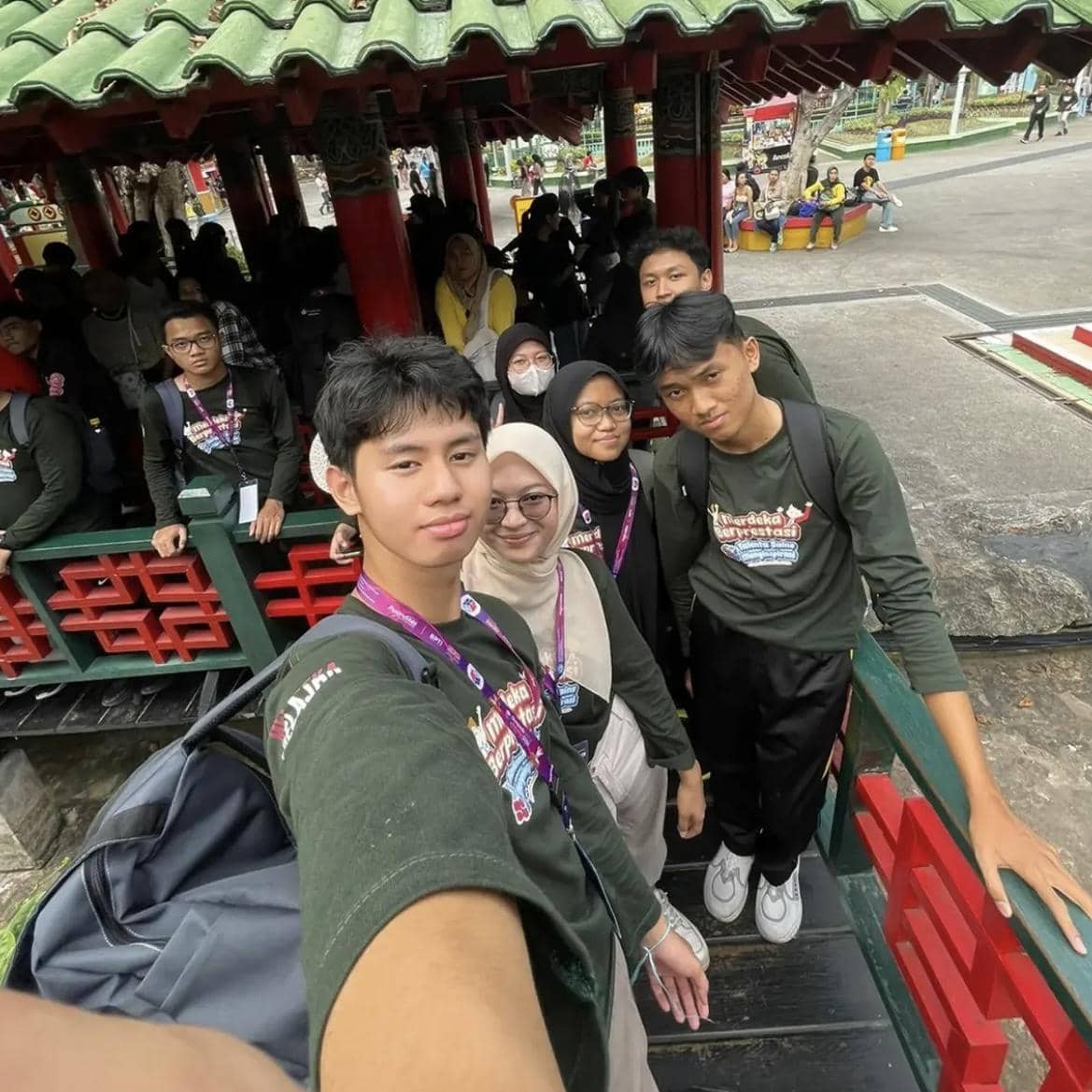 Sekelompok anak muda mengenakan kaus hijau bertuliskan acara Kafka Clash of Champions Season 3 berfoto bersama di area taman dengan bangunan bergaya oriental.