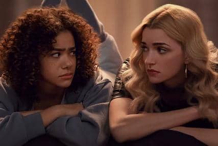 Dua perempuan berbaring berdampingan di atas tempat tidur, saling menatap dengan ekspresi serius dalam adegan serial Ginny & Georgia.